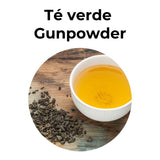 Té verde Gunpowder en hojas junto a taza de infusión dorada sobre superficie de madera.