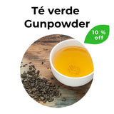 Té verde Gunpowder en hojas junto a taza de infusión dorada sobre superficie de madera. Se encuentra con un 10 % de descuento.